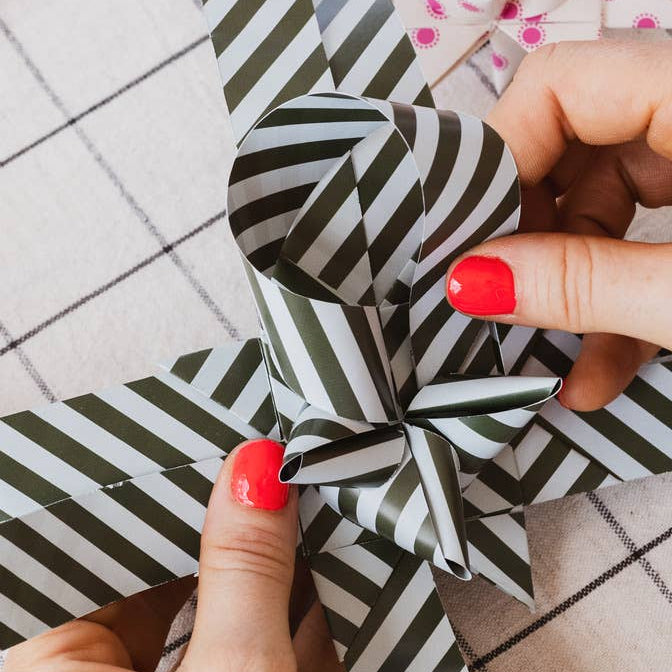 Person holding a black and white striped paper flower on a tiled floor.