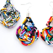 A pair of colorful fabric dangle earrings with a braided knot design and silver fishhook wires, displayed on a clean white background.