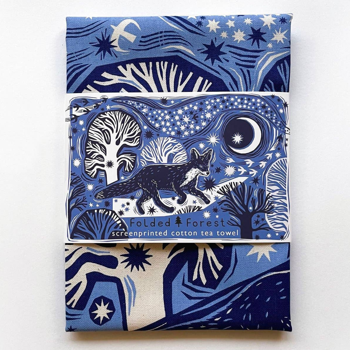 Folded forest-themed tea towel with blue and white design on a white background