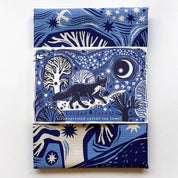 Folded forest-themed tea towel with blue and white design on a white background