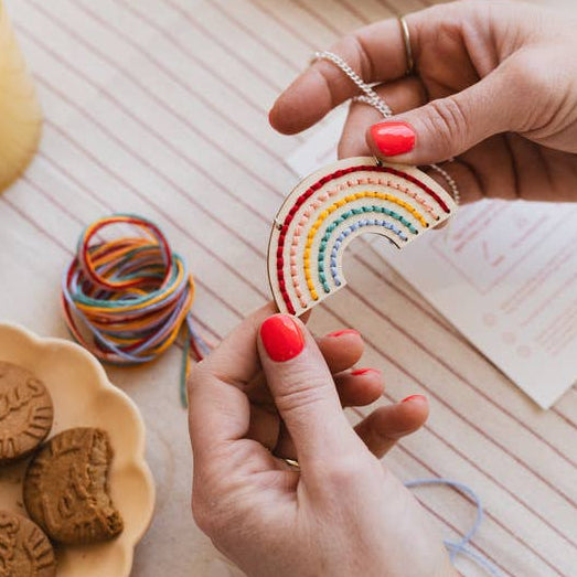Person holding a rainbow-themed cookie cutter on a table with cookies, a mug, and a candle.