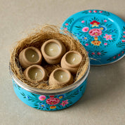Decorative tin with floral design containing small ceramic eggs on a beige background