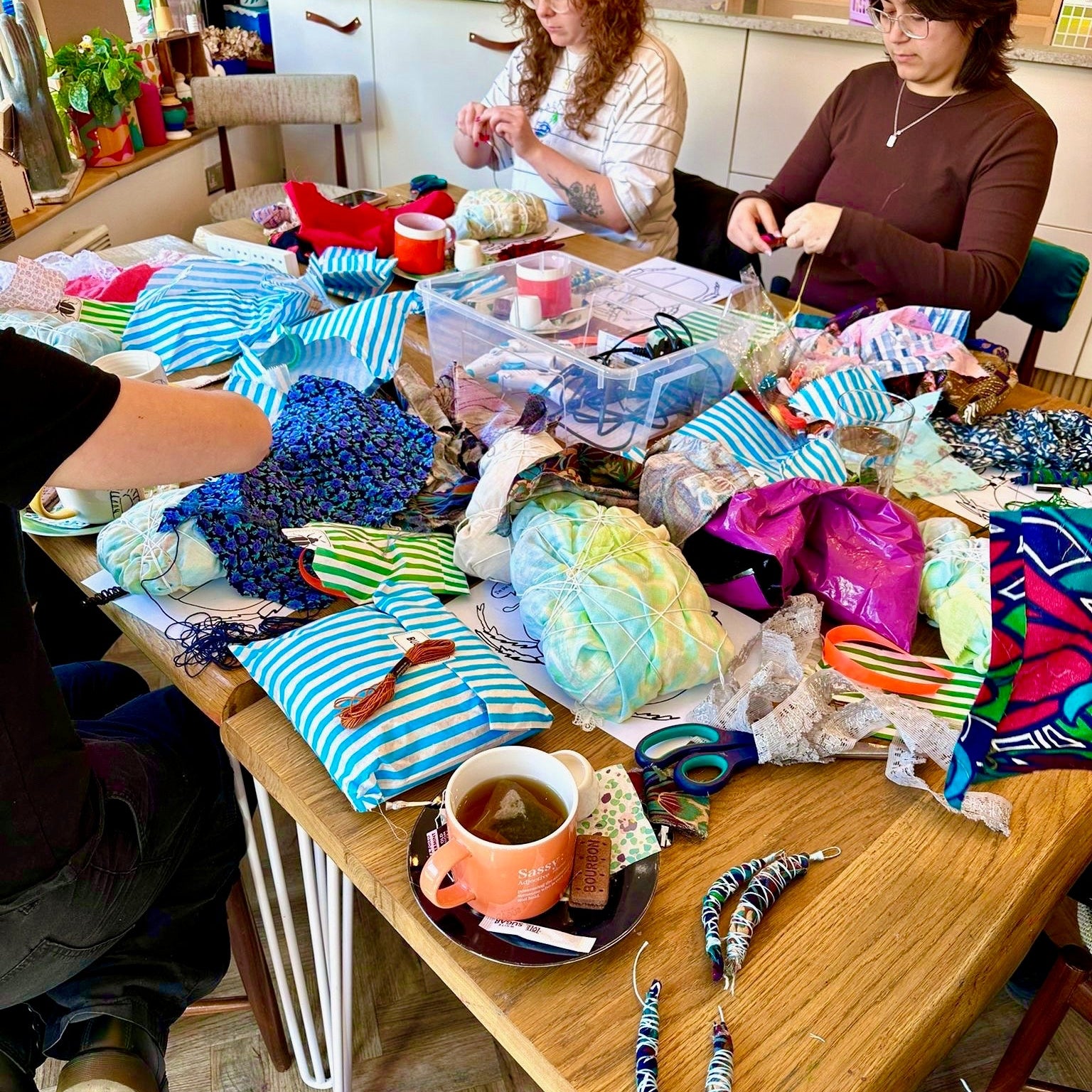 Two women sitting at a table with craft materials and a cup of tea.