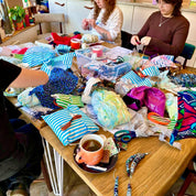 Two women sitting at a table with craft materials and a cup of tea.