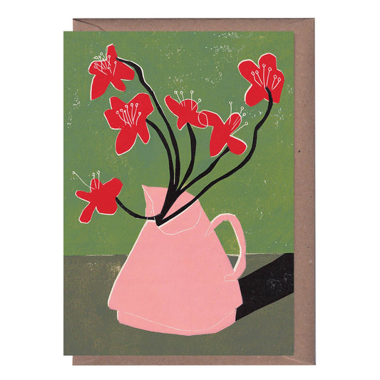 A greeting card with a linocut print of red flowers in a pink vase on a green background, accompanied by a kraft envelope.