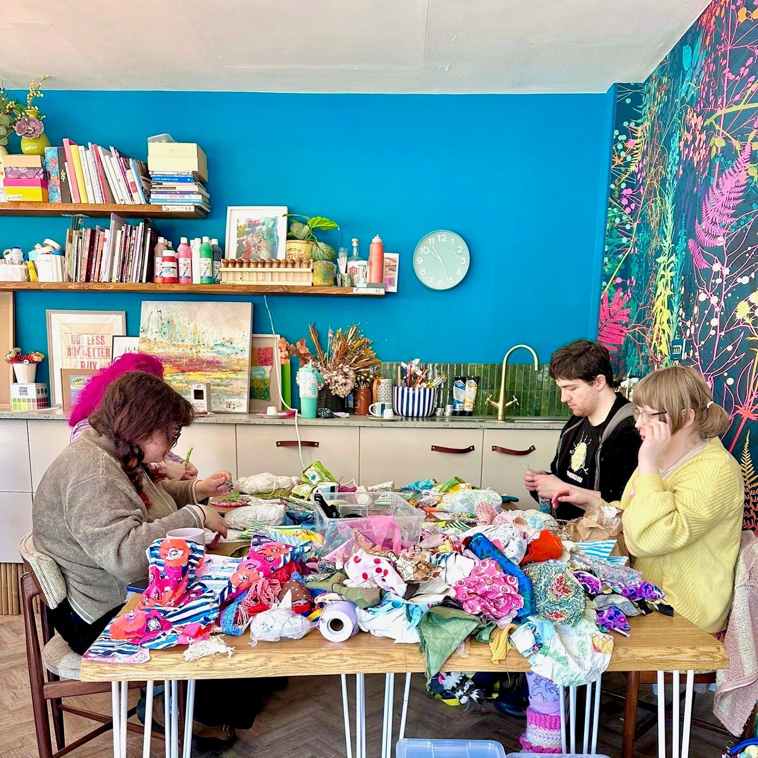 Three people sitting around a table with toys and containers in a colorful room.