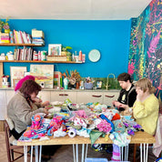 Three people sitting around a table with toys and containers in a colorful room.