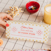 Cotton Clara 3D paper stars kit on a checkered tablecloth with scissors and a candle.