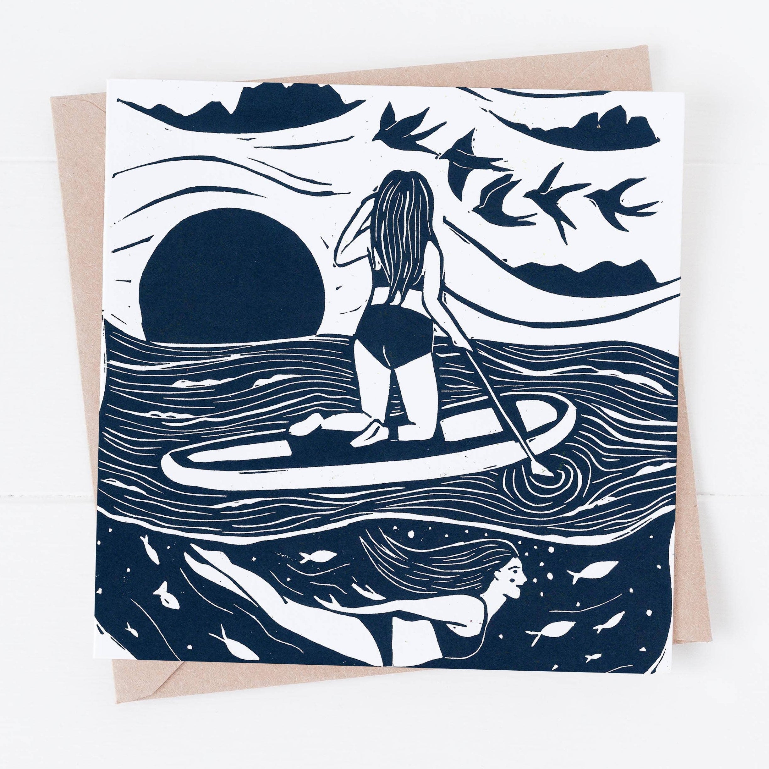 Greeting card with illustration of a person paddleboarding on a wave, surrounded by birds and mountains.