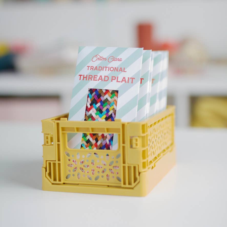 Yellow crate with colorful thread plait book inside on a white surface