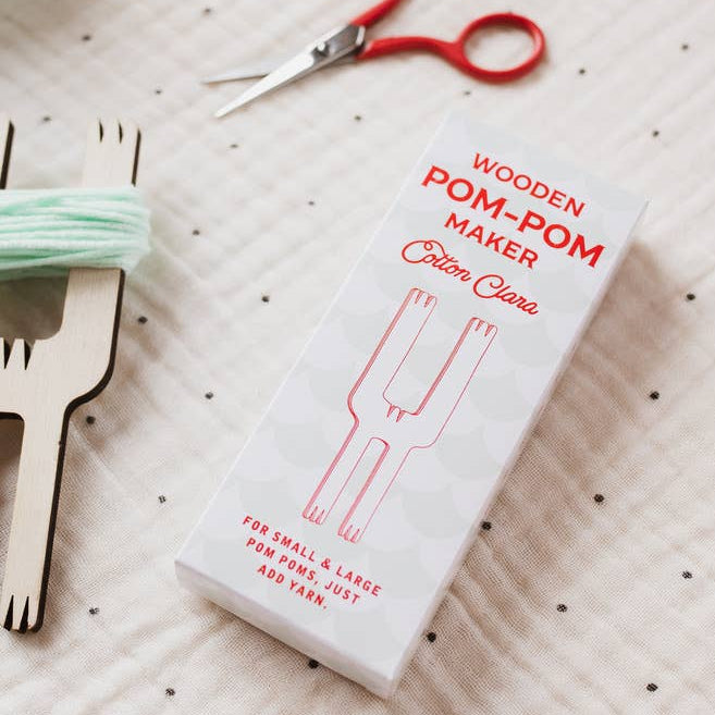 Wooden pom-pom maker with packaging on a polka dot fabric background