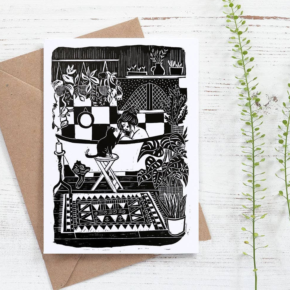Greeting card with black and white illustration of a couple kissing, envelope, and plants on a light wooden surface.
