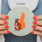 Person holding a cross-stitched hoop with a squirrel design.