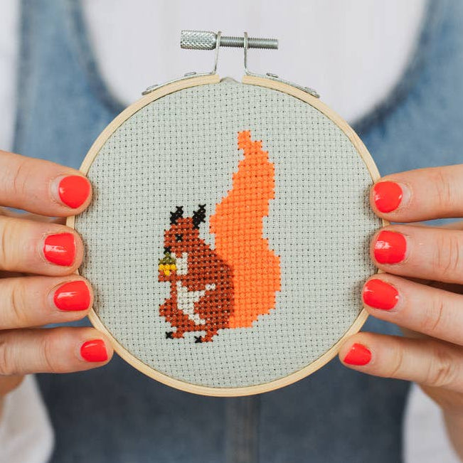 Person holding a cross-stitched hoop with a squirrel design.