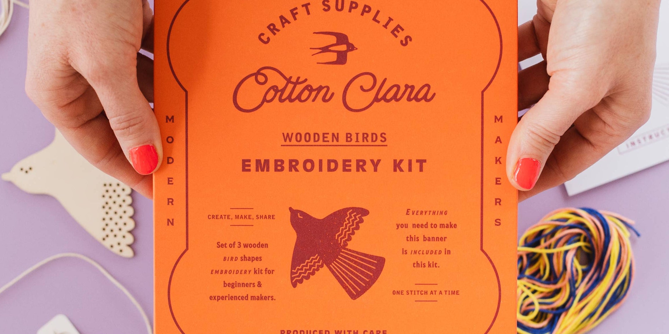 Cotton Clara wooden birds embroidery kit on a purple background with craft supplies.