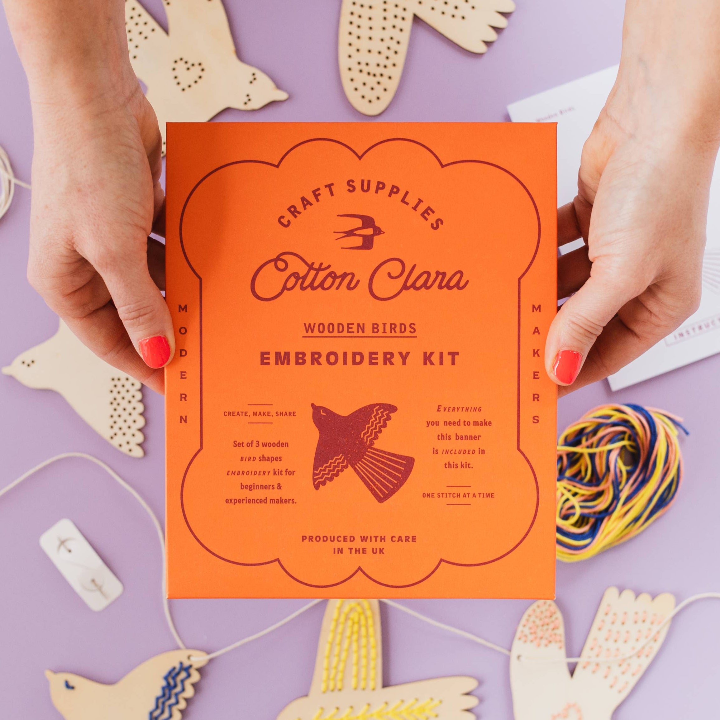 Cotton Clara wooden birds embroidery kit on a purple background with craft supplies.