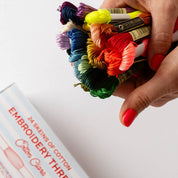 Hand holding colorful embroidery thread skeins with a box of embroidery thread in the foreground.
