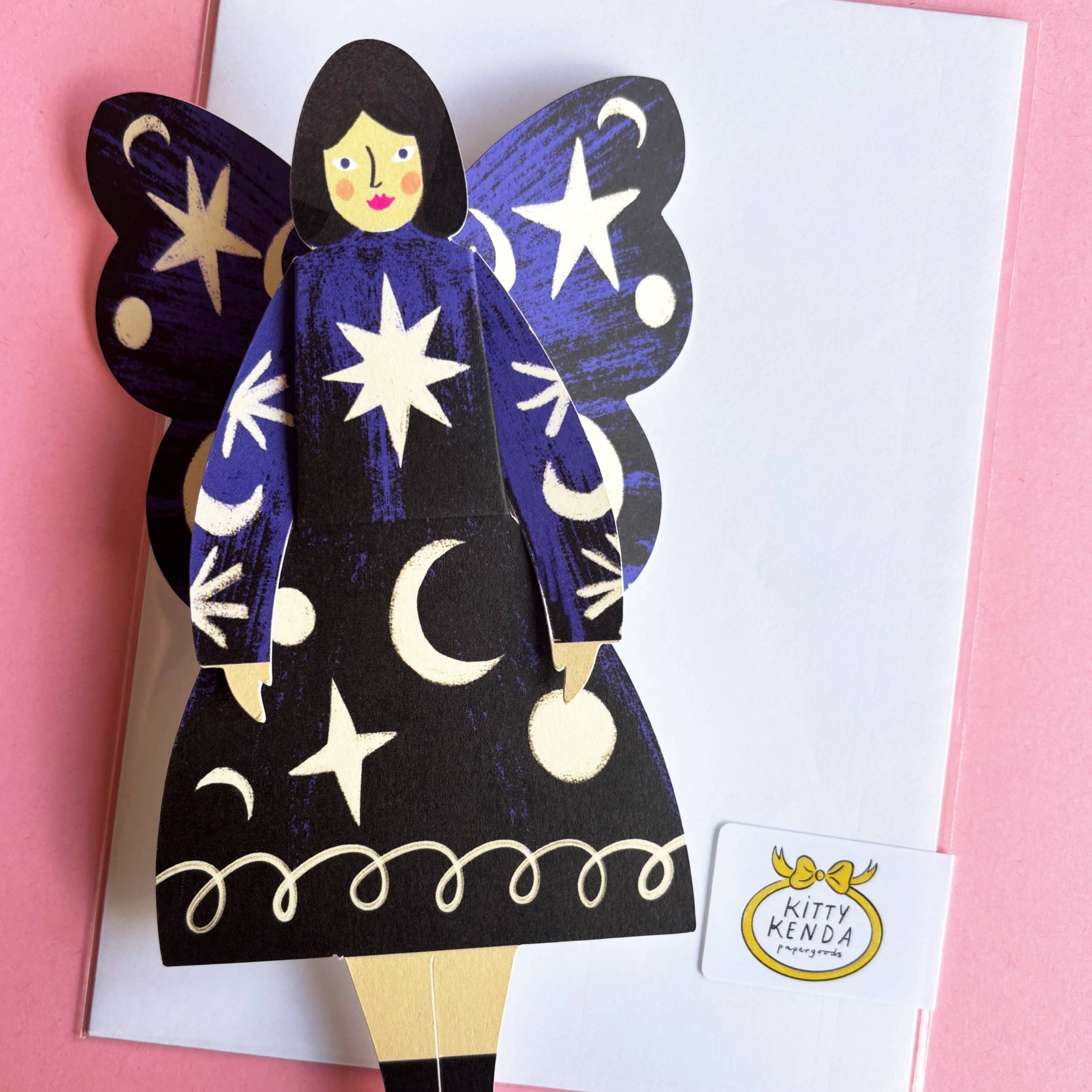 Butterfly-shaped paper doll with star and moon designs on a pink background