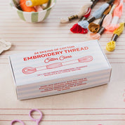 Box of embroidery thread with spools and scissors on a wooden surface