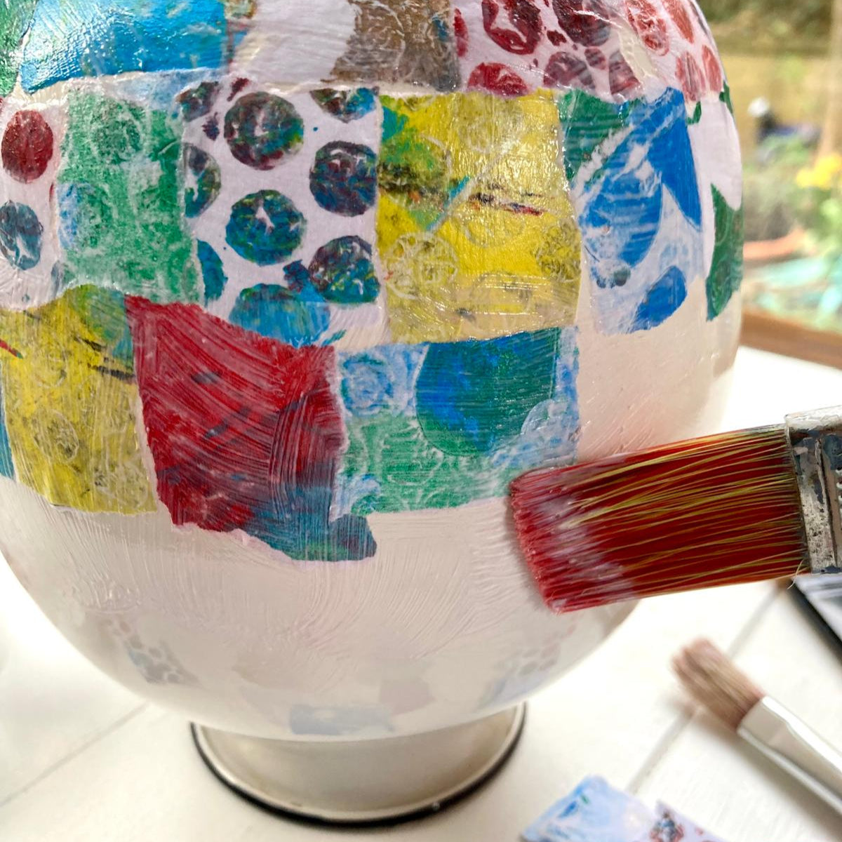 A craft activity in progress with a painted globe and colorful paper cutouts, with a paintbrush and other crafting materials scattered around.
