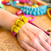 Hand wearing a yellow bracelet with colorful beads on a cork board background