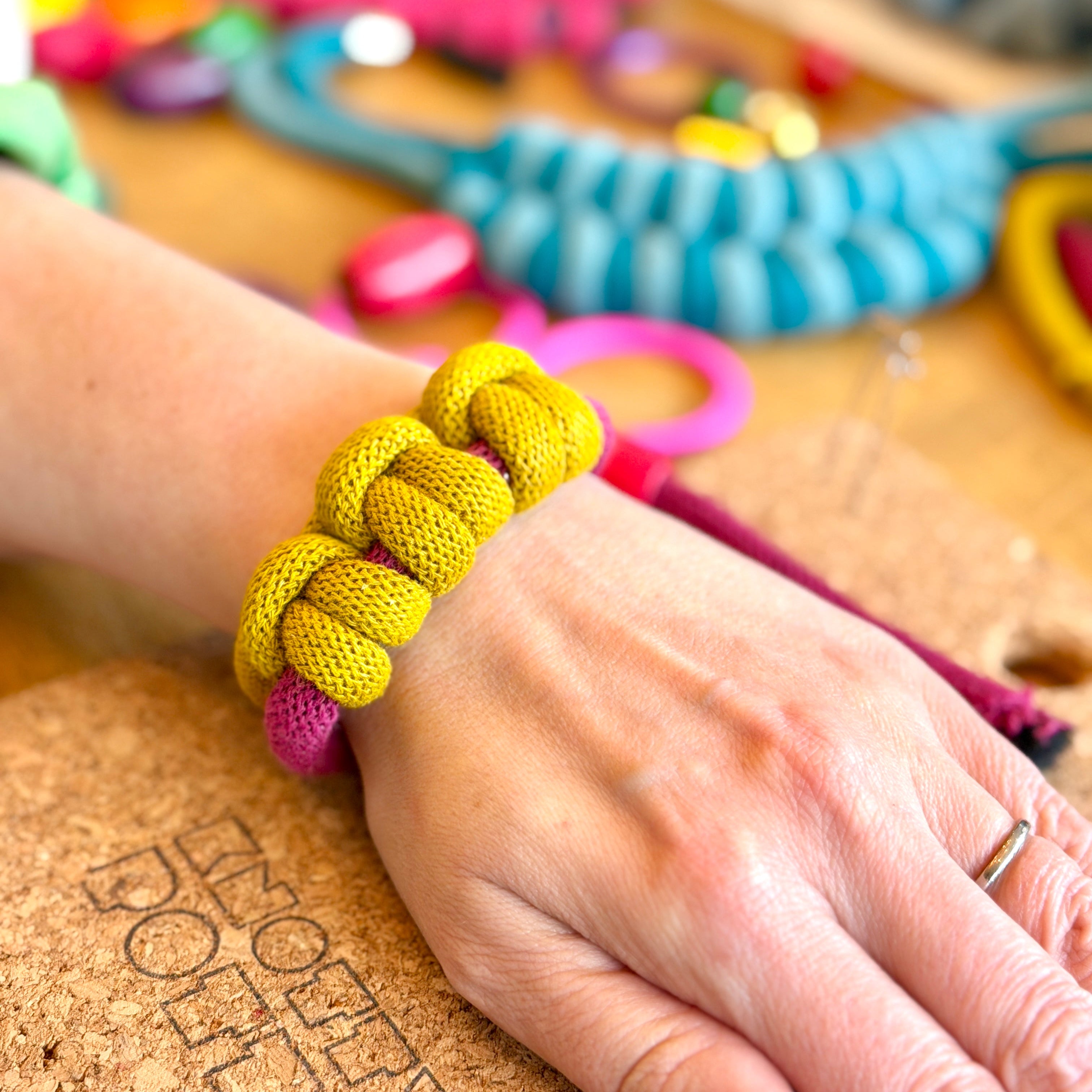 Hand wearing a yellow bracelet with colorful beads on a cork board background