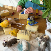 Woman working on small animal figures at a table with various materials and tools.