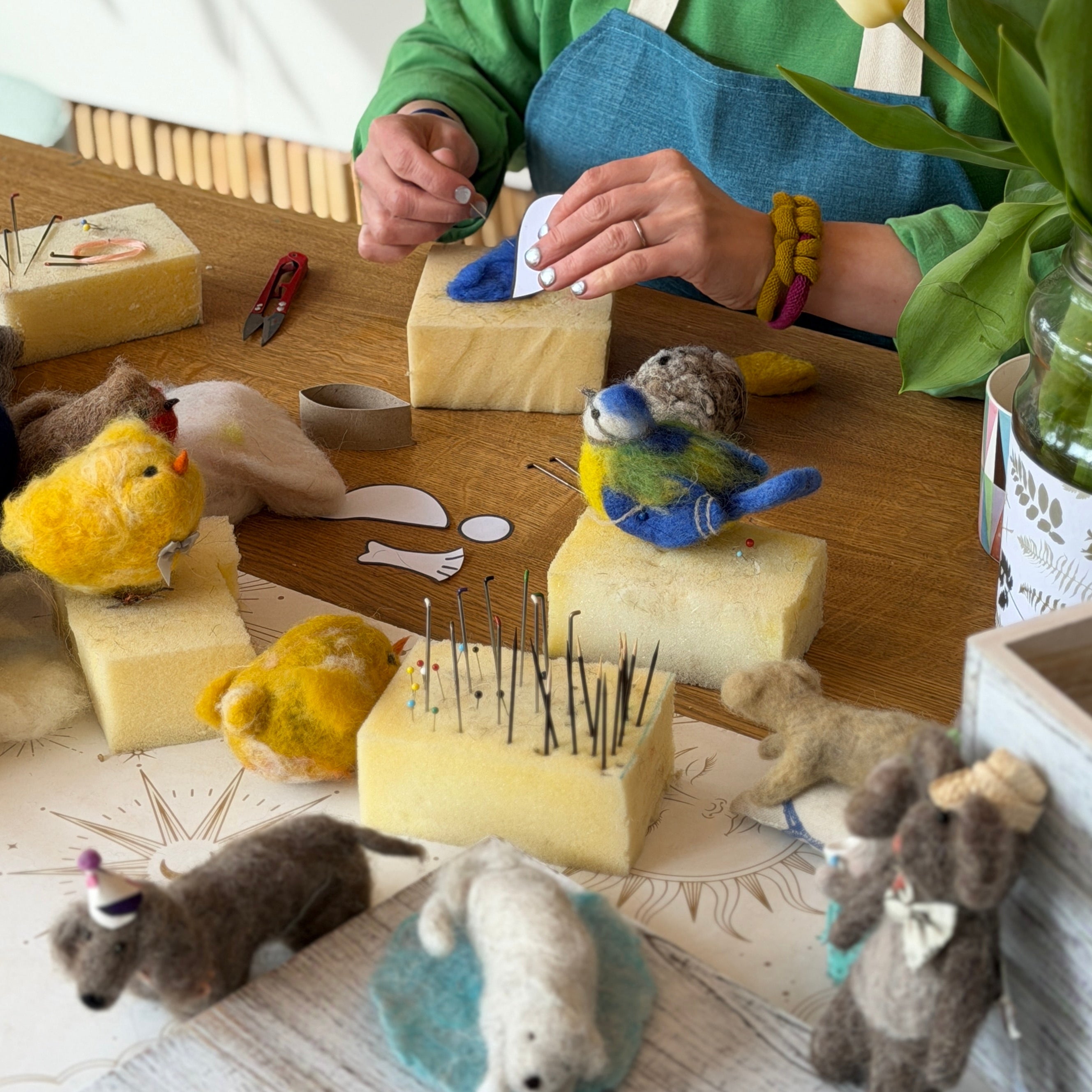 Woman working on small animal figures at a table with various materials and tools.