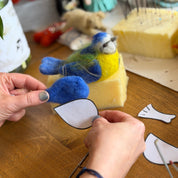 Person crafting a felt bird toy on a wooden surface with various craft materials.