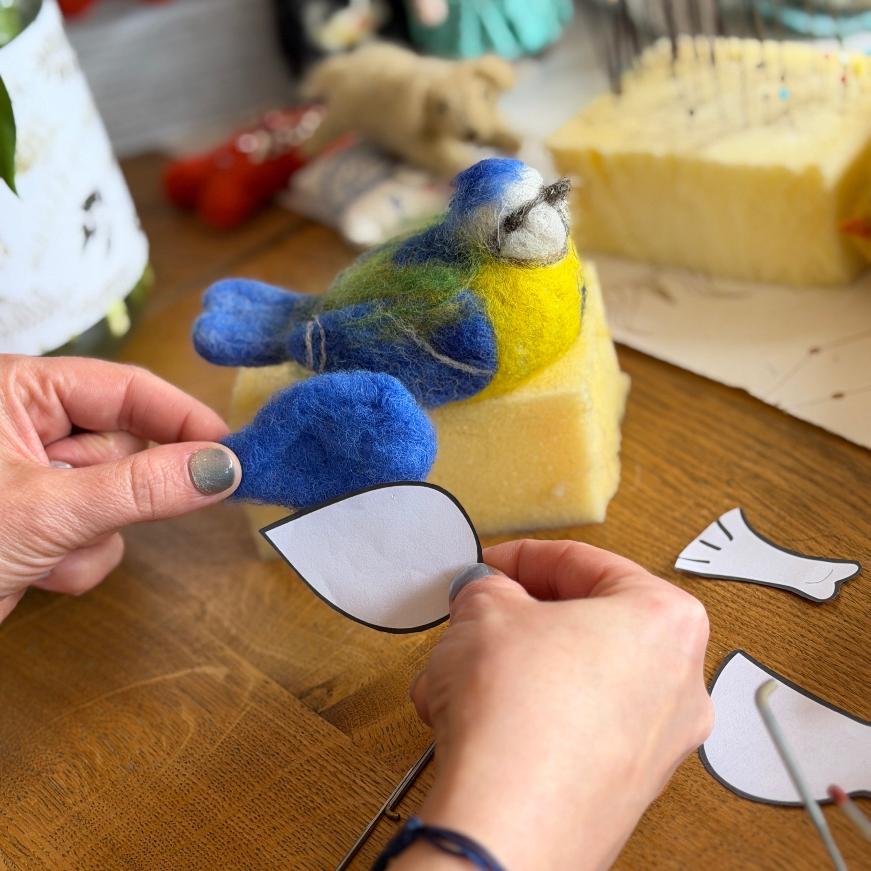 Person crafting a felt bird toy on a wooden surface with various craft materials.