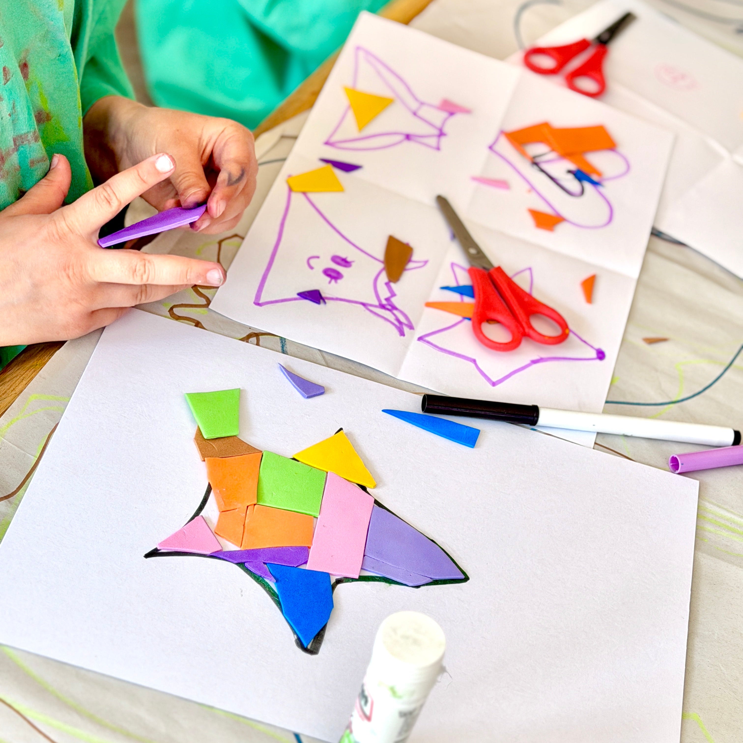 Children's art project with colorful shapes and markers on a table.