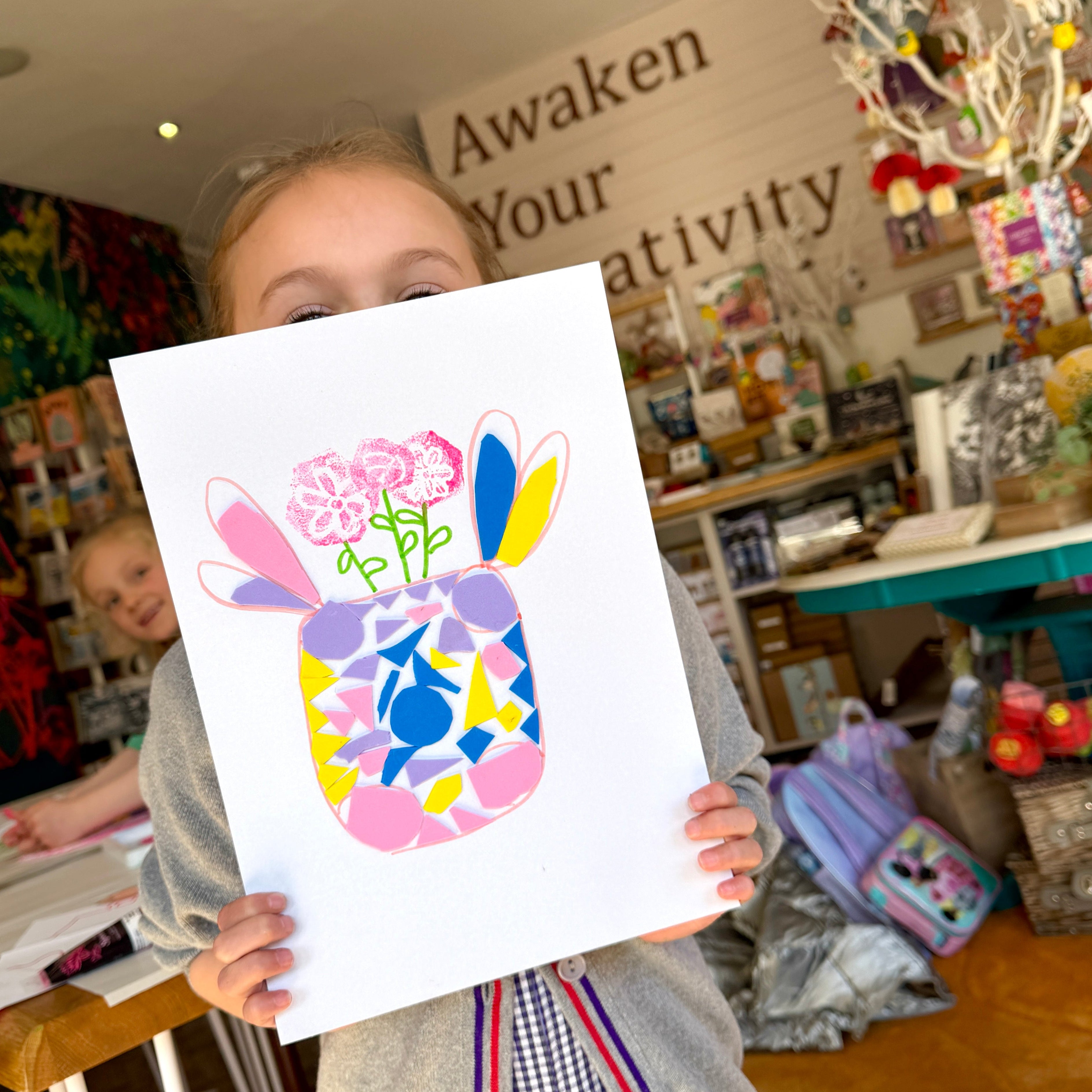 Child holding a colorful handprint art in a store with 'Awaken Your Creativity' sign.
