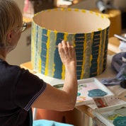 Person painting a large cylindrical object with blue and yellow patterns in a workshop setting.