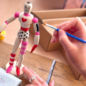 Person painting a small figurine with a brush on a wooden table.