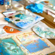 Artistic watercolor paintings on paper with a paintbrush and watercolor pan on a wooden table.