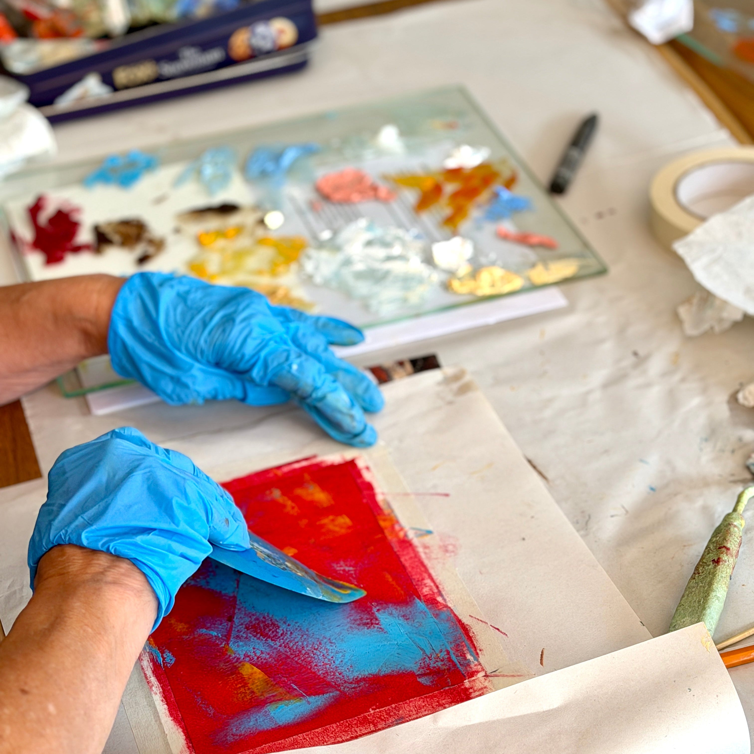 Person wearing blue gloves working on a colorful art project with various materials on a table.