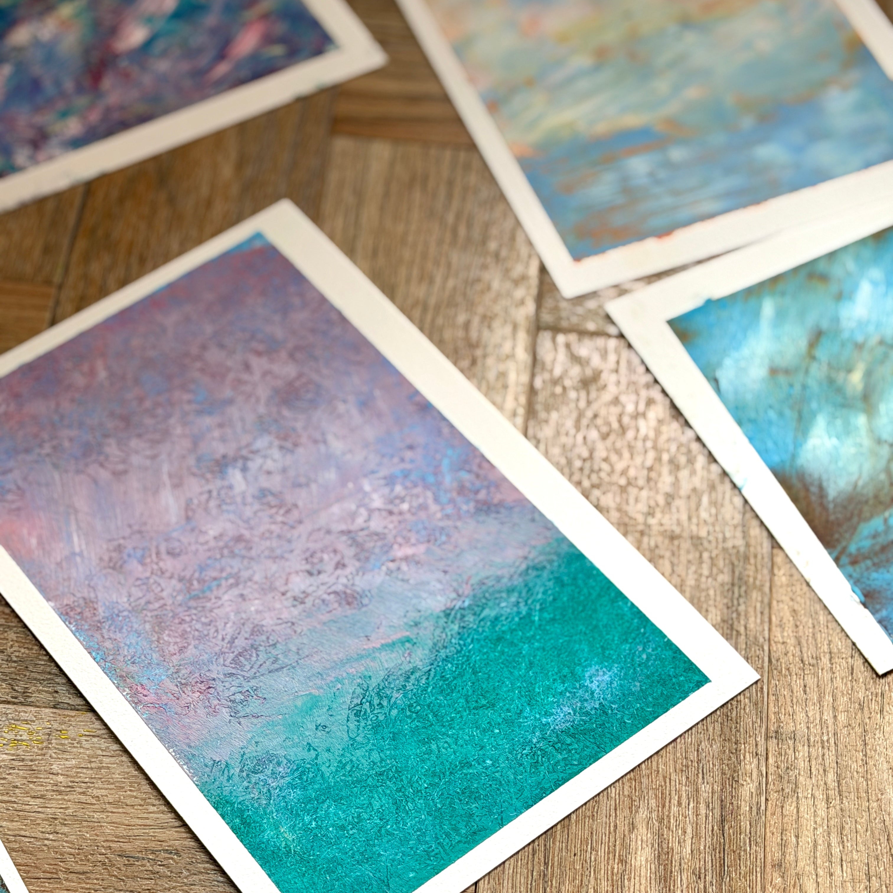 Colorful abstract paintings on paper scattered on a wooden surface