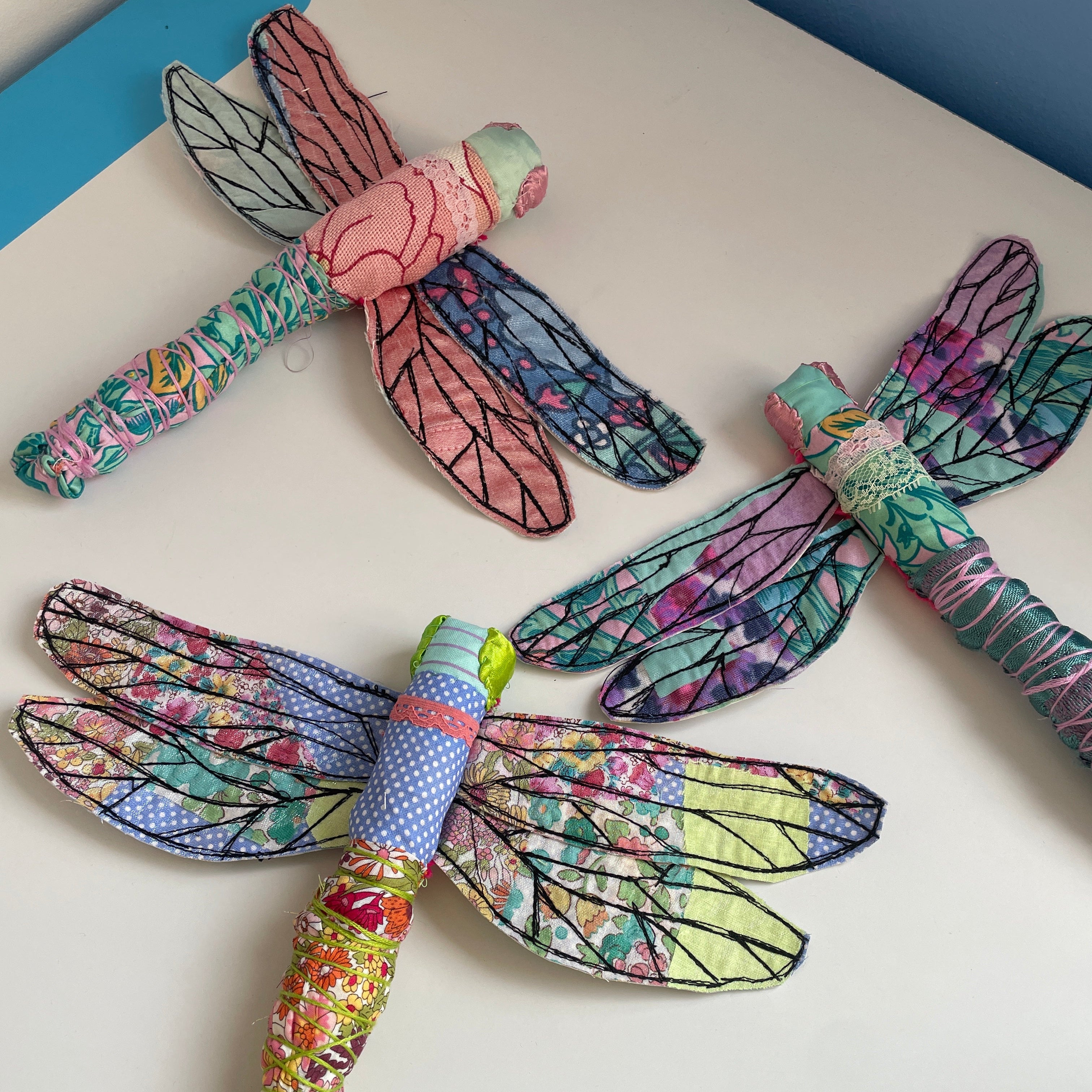 Colorful dragonfly-shaped toys on a white surface with a ruler for scale.