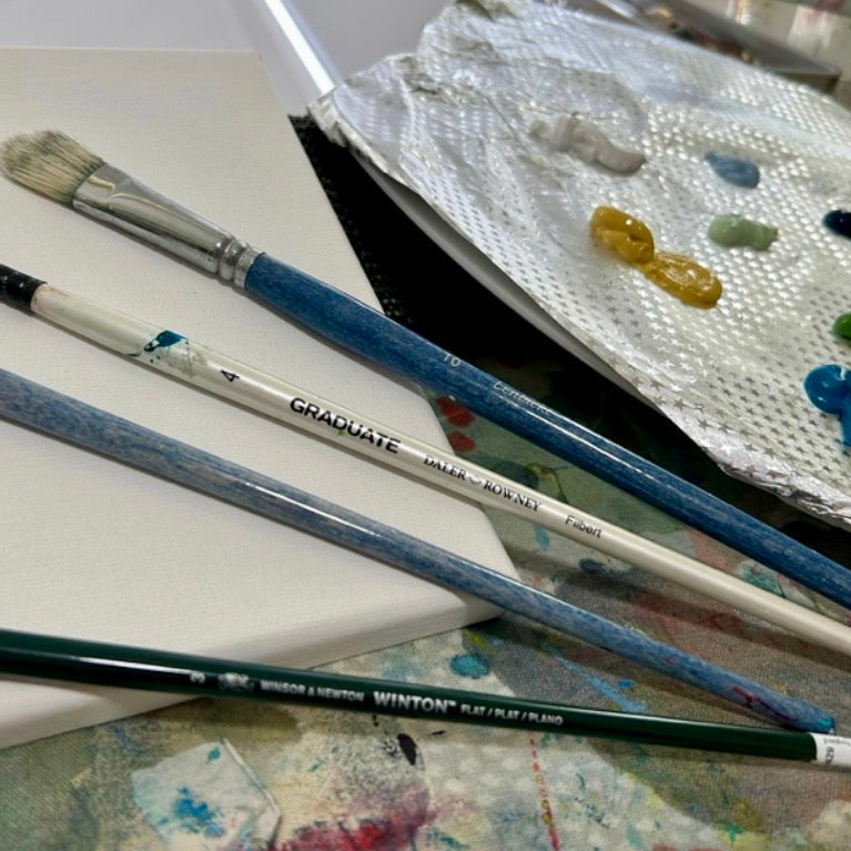 Art supplies including paintbrushes and a palette with paint on a table.