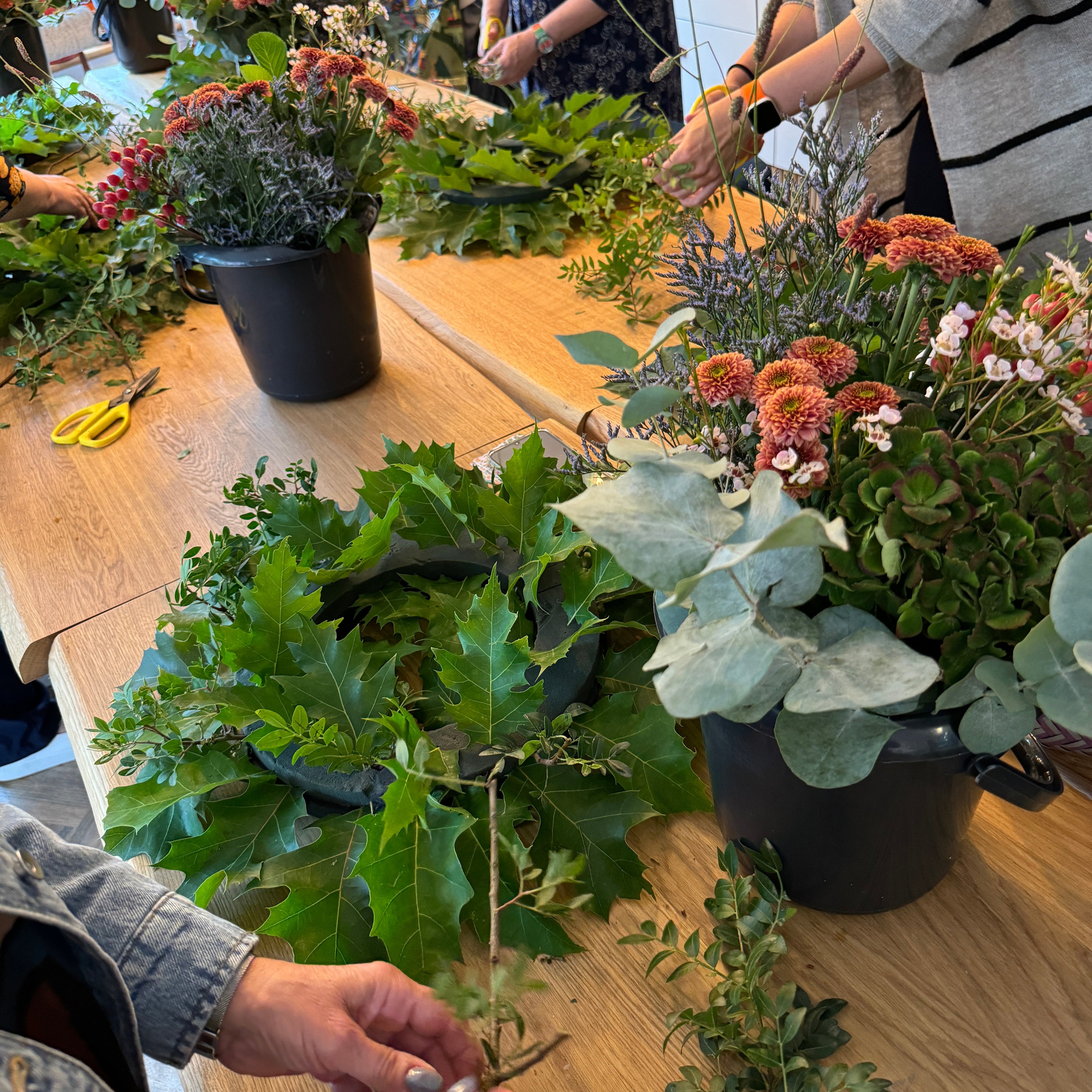 People arranging flowers on a wooden table with a focus on floral design.