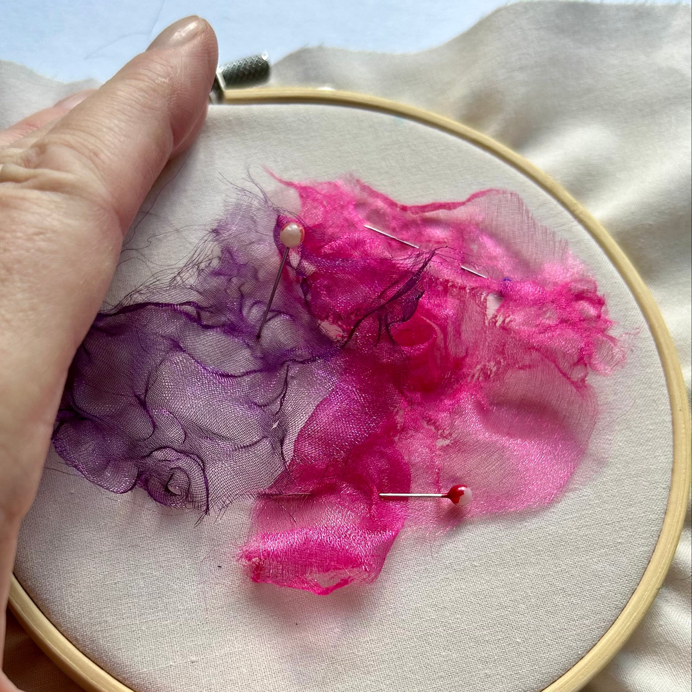 Hand holding an embroidery hoop with pink and purple fabric on a light background