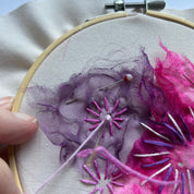 Embroidery hoop with pink and purple floral embroidery on a light blue background