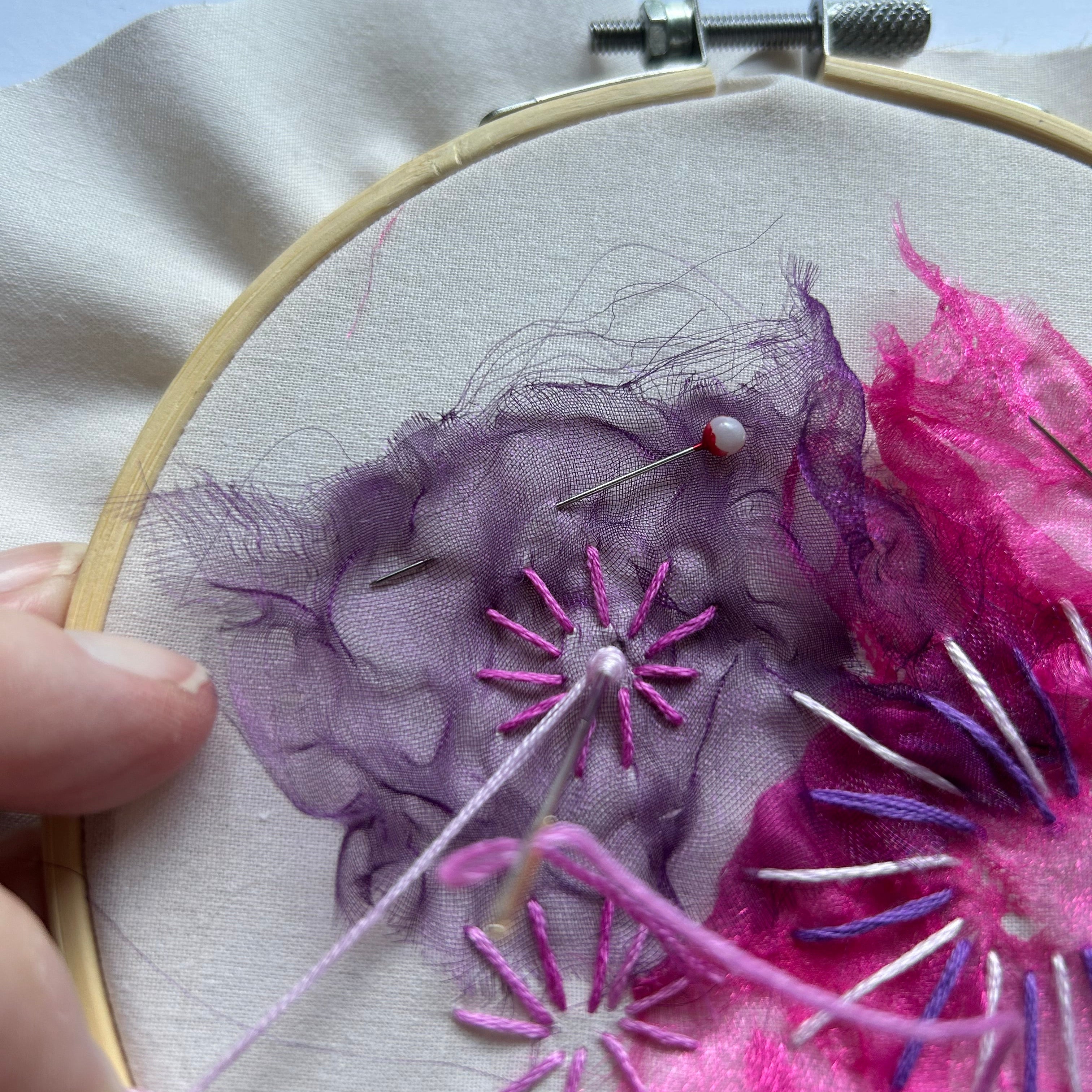 Embroidery hoop with pink and purple floral embroidery on a light blue background