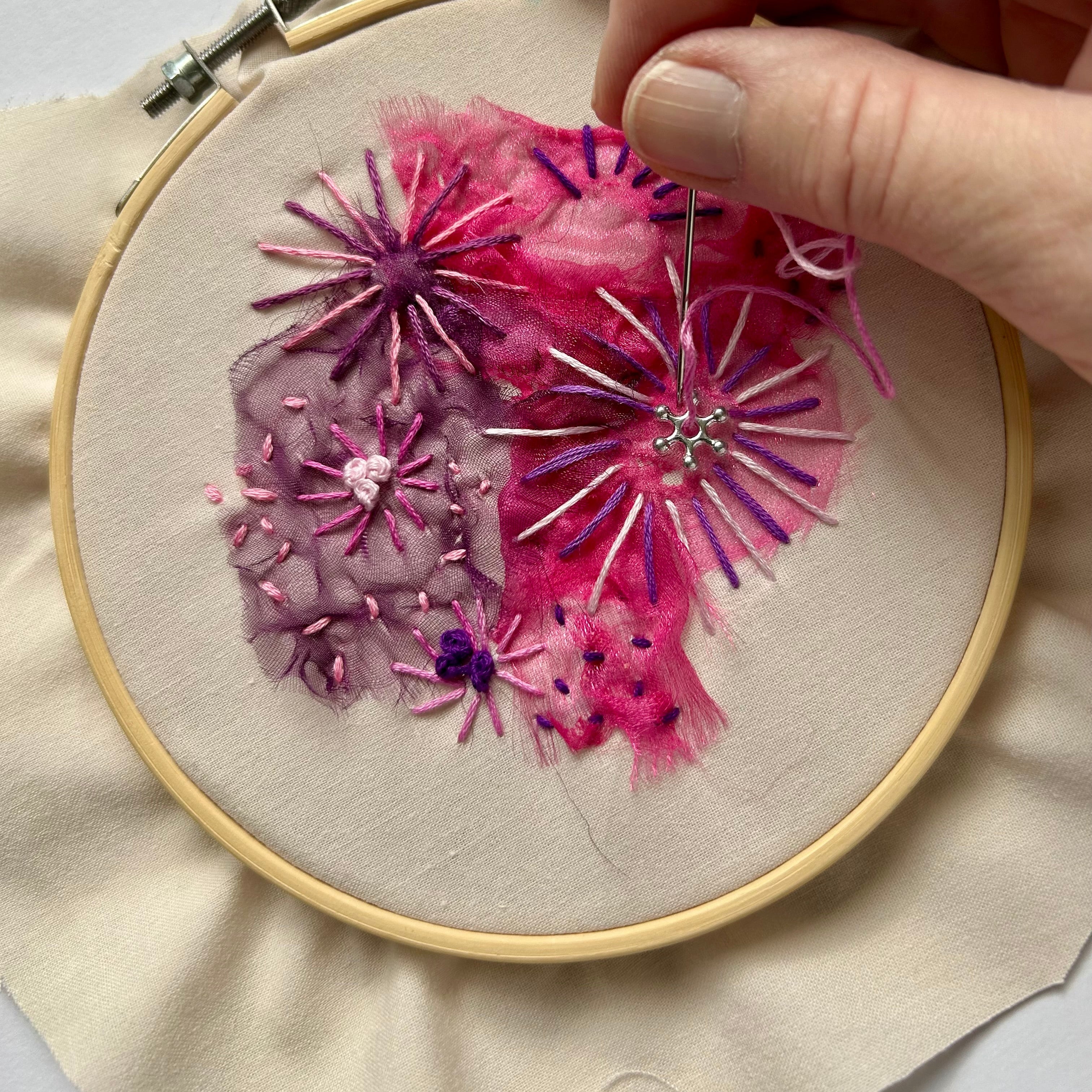 Embroidery hoop with pink floral design being worked on.