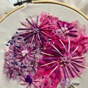 Embroidery hoop with pink and purple floral embroidery on a beige fabric background