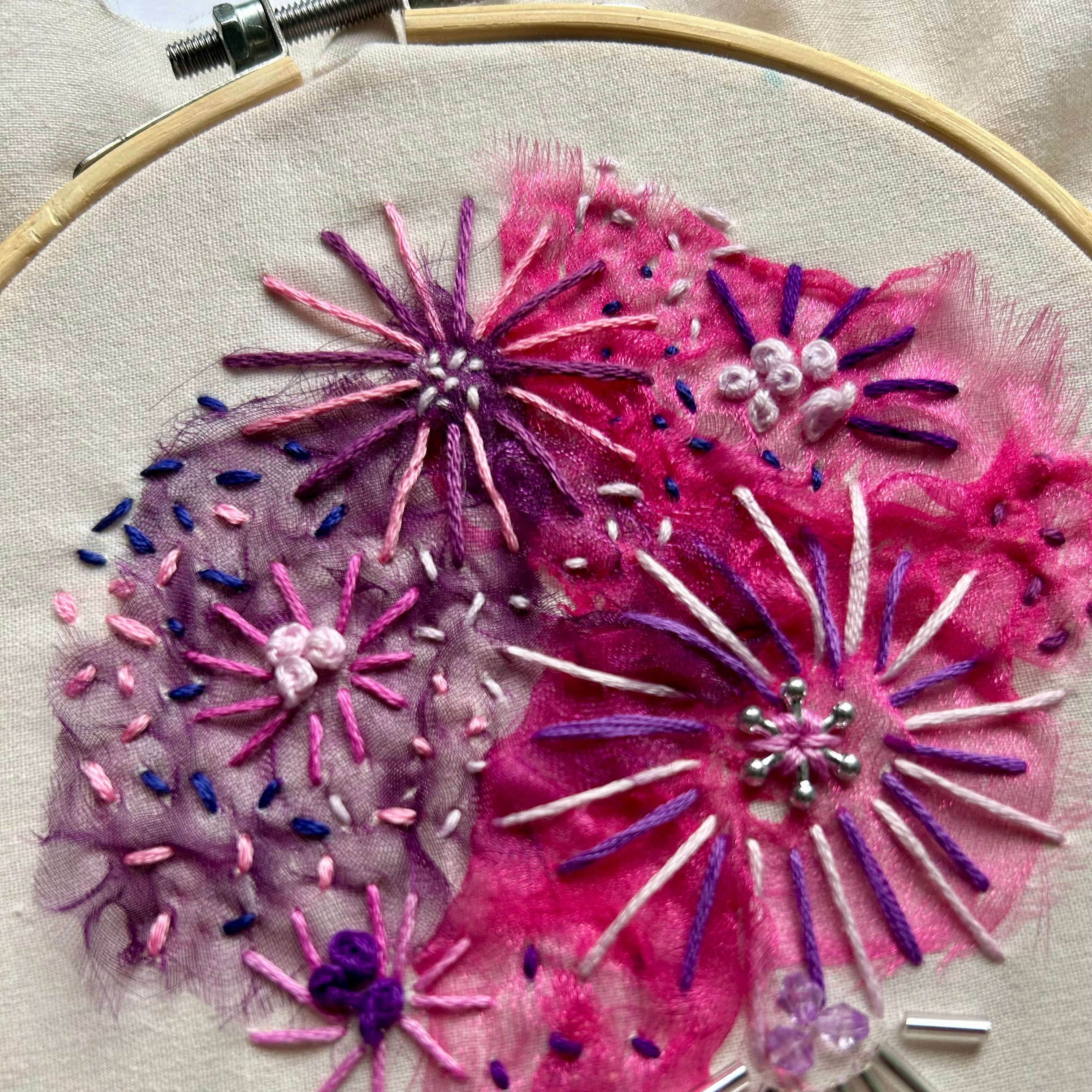 Embroidery hoop with pink and purple floral embroidery on a beige fabric background