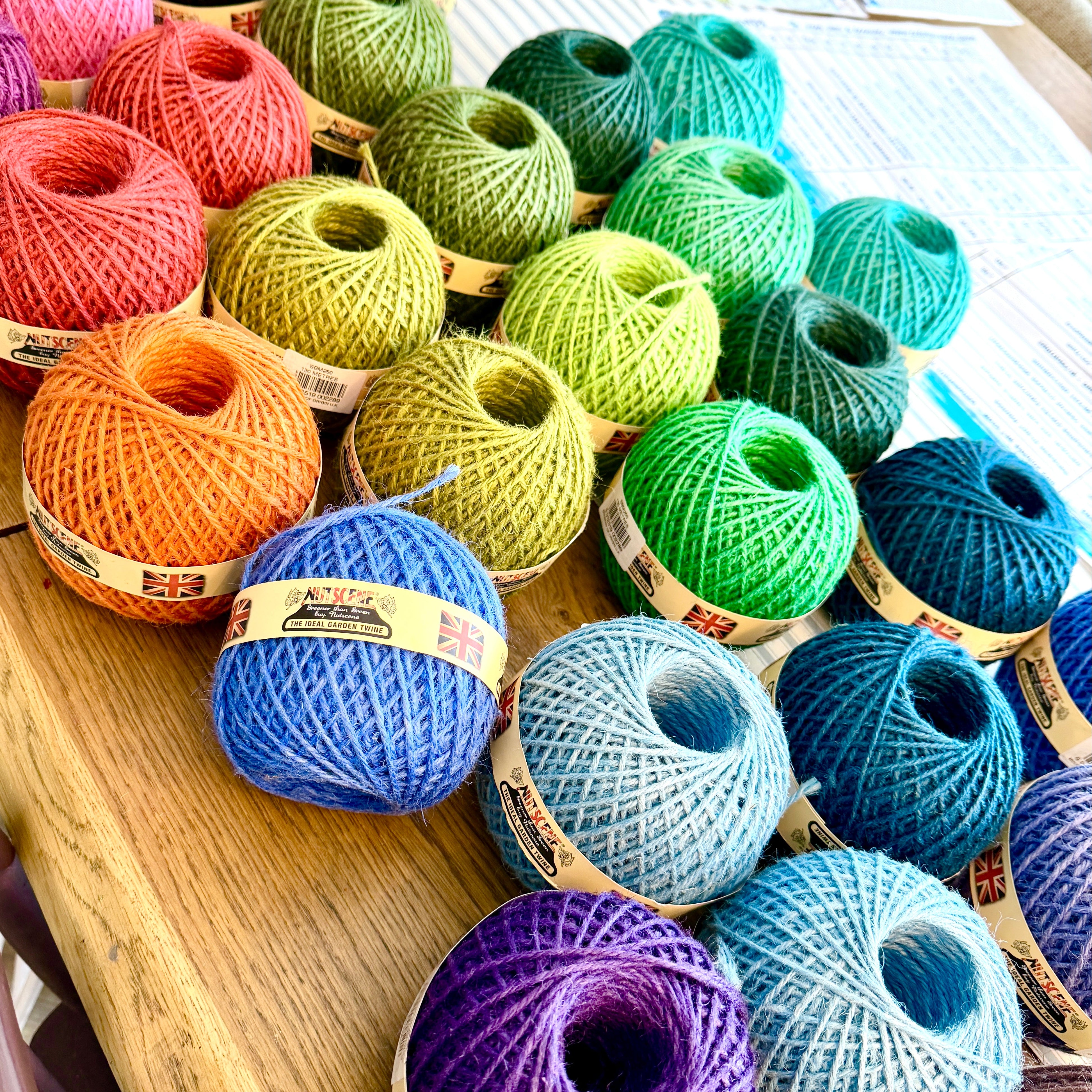 A collection of colorful yarn skeins in various colors including pink, green, orange, blue, purple, and black, arranged on a wooden table.