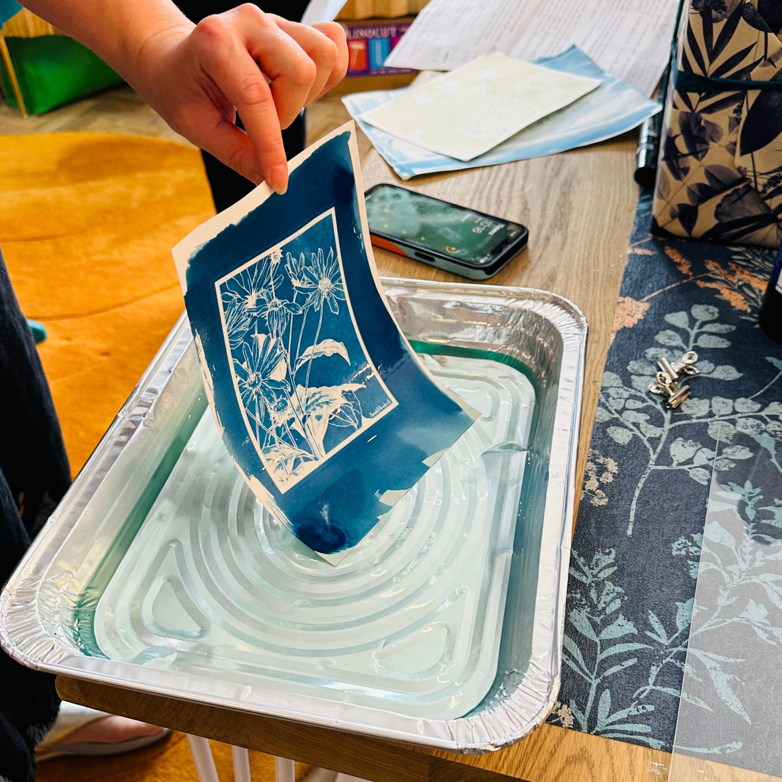 Person holding a blue ceramic dish over a tray of water on a wooden table.