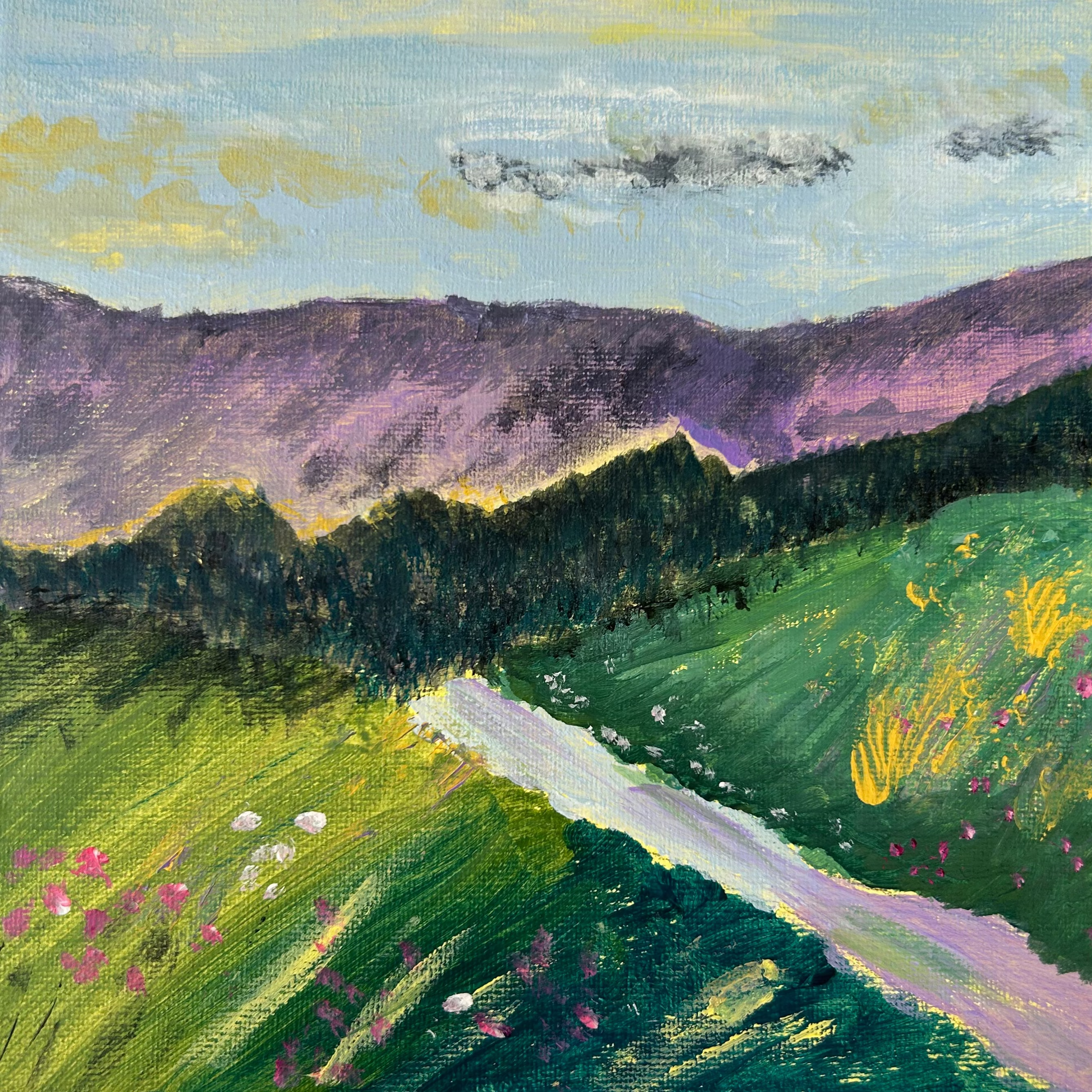 A square canvas painting of a mountain landscape with green fields, purple mountains, and a pale sky, photographed on top of white paper with paint marks around it.