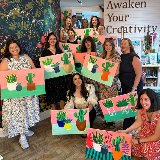 Group of people with their artwork in a room with 'Awaken Your Creativity' sign.